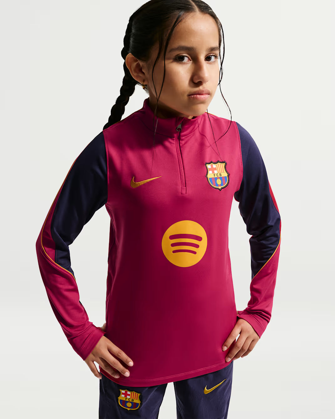 A young girl wearing a Nike FC Barcelona long-sleeve training top in magenta and navy blue, featuring the club crest and a yellow Spotify sponsor logo on the front.