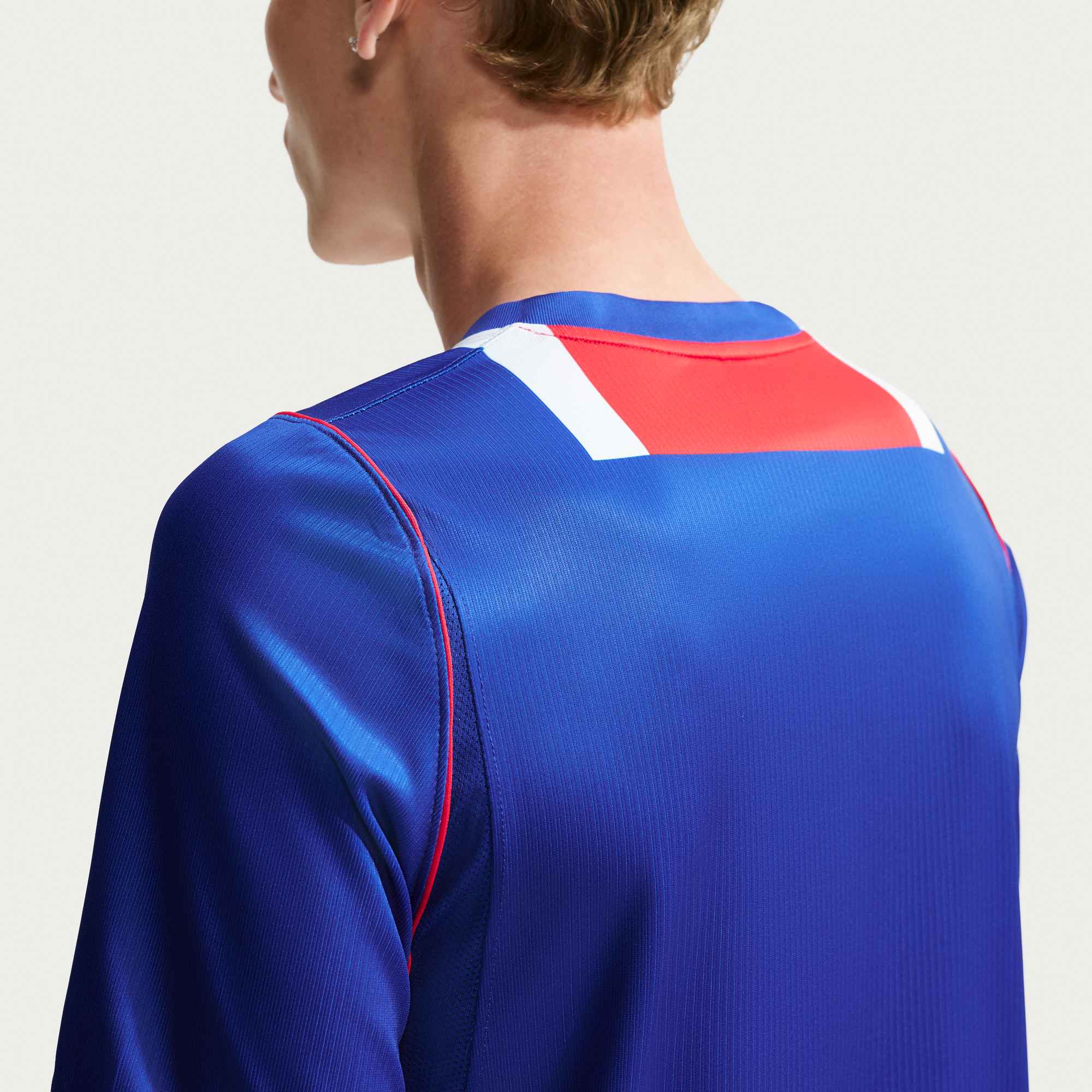 Blue athletic shirt with red and white accents on a plain background