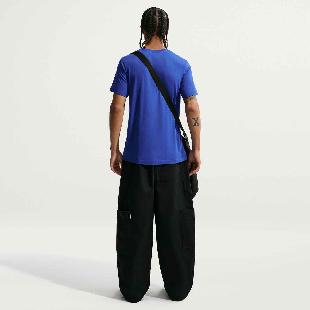 Person wearing a blue t-shirt and black pants with a black strap over the shoulder on a white background
