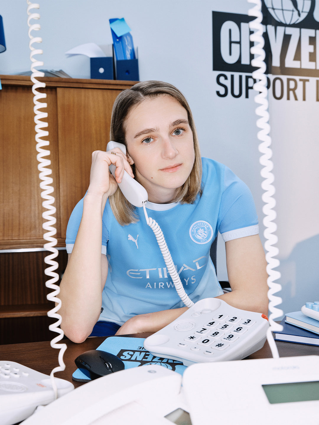 Vivian Miedema wearing a blue sports jersey with a phone headset in an office setting